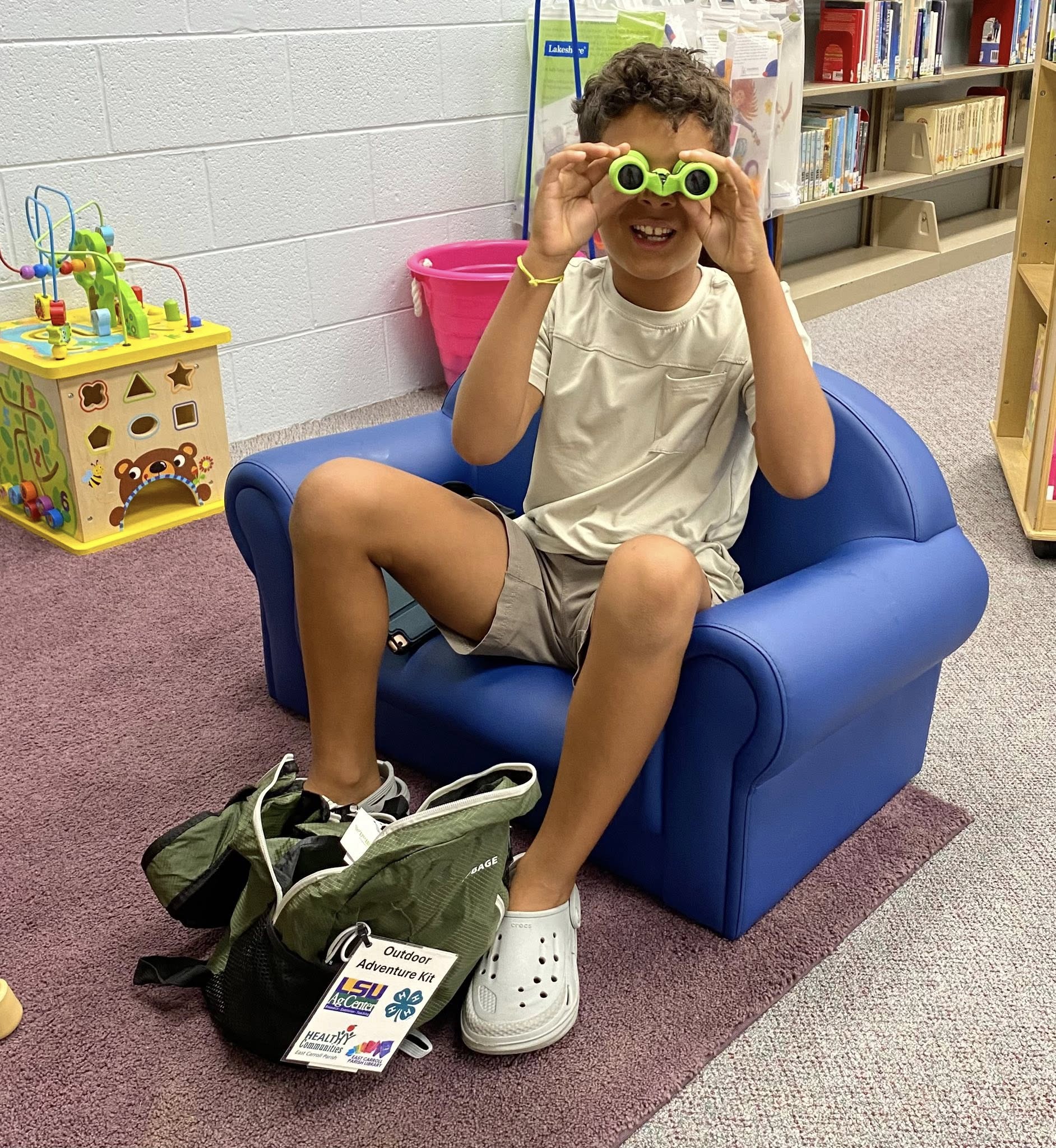 A boy sitting in a chair looking through a small pair of binoculars.